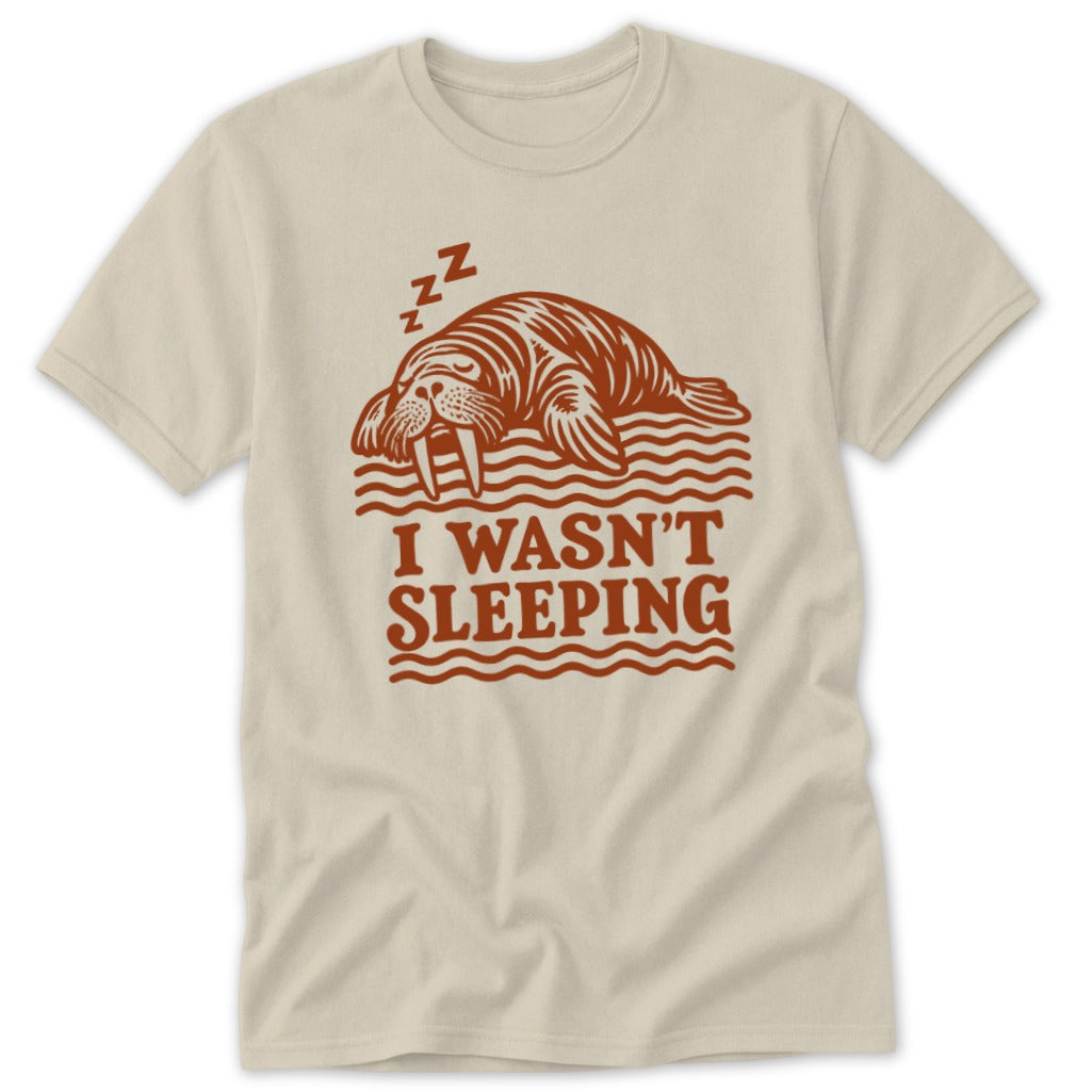 Beige short-sleeve t-shirt with a brown graphic of a sleeping walrus and the text I WASN'T SLEEPING.