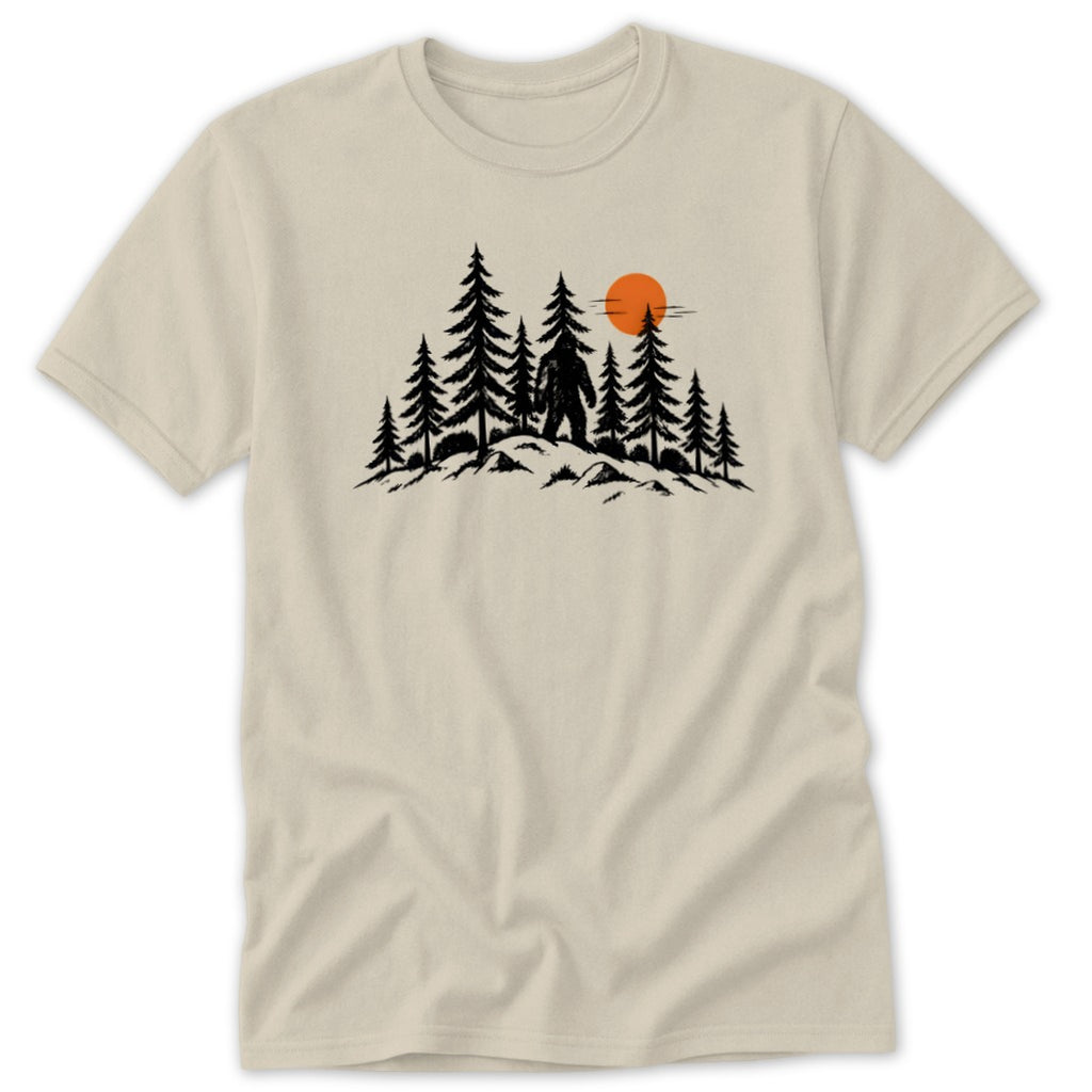 Black Bigfoot silhouette among pine trees with orange sun on a cream t-shirt.