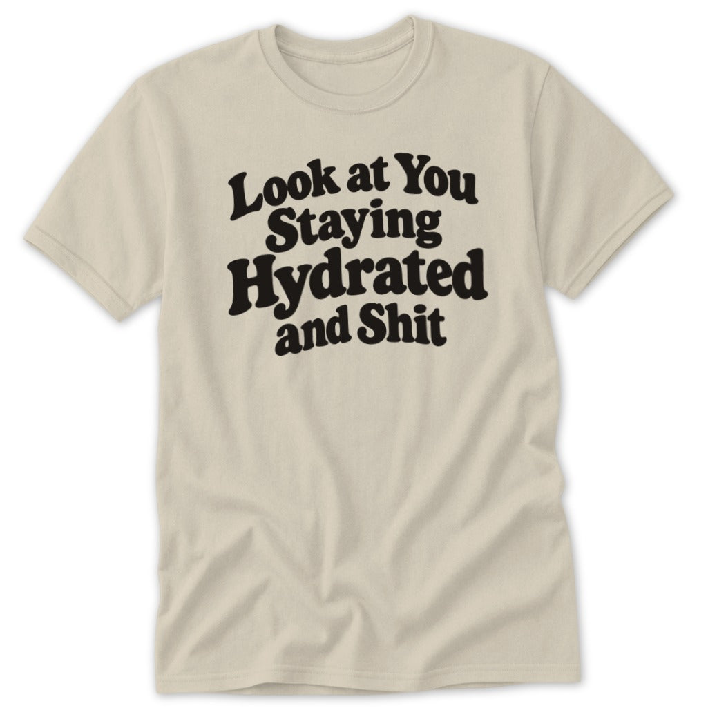 Beige t-shirt featuring bold black text on the chest that reads Look at You Staying Hydrated and Shit.