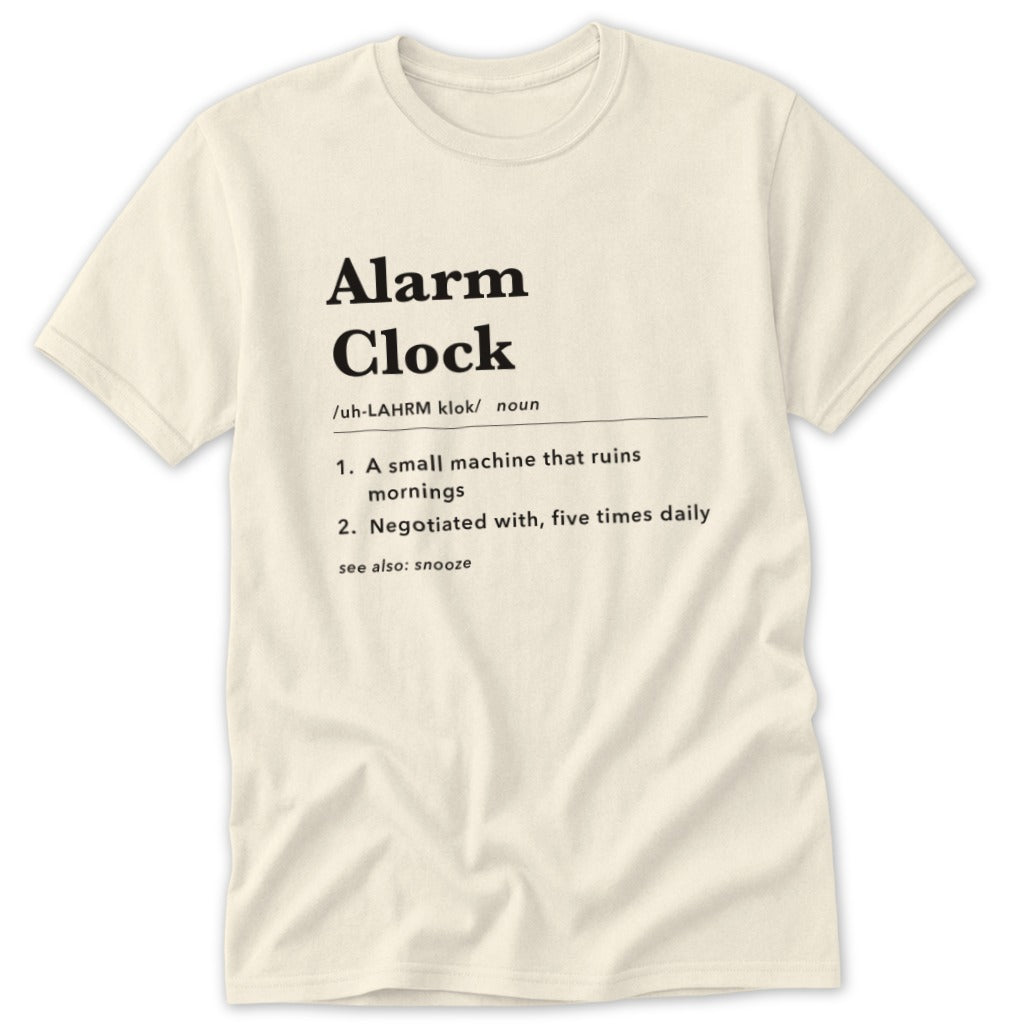 Cream t-shirt with "Alarm Clock" definition: "small machine that ruins mornings," "negotiated with, five times daily."