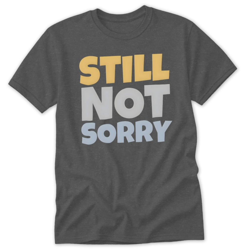 A dark gray crewneck t-shirt featuring the stacked text STILL NOT SORRY in yellow, light gray, and light blue.