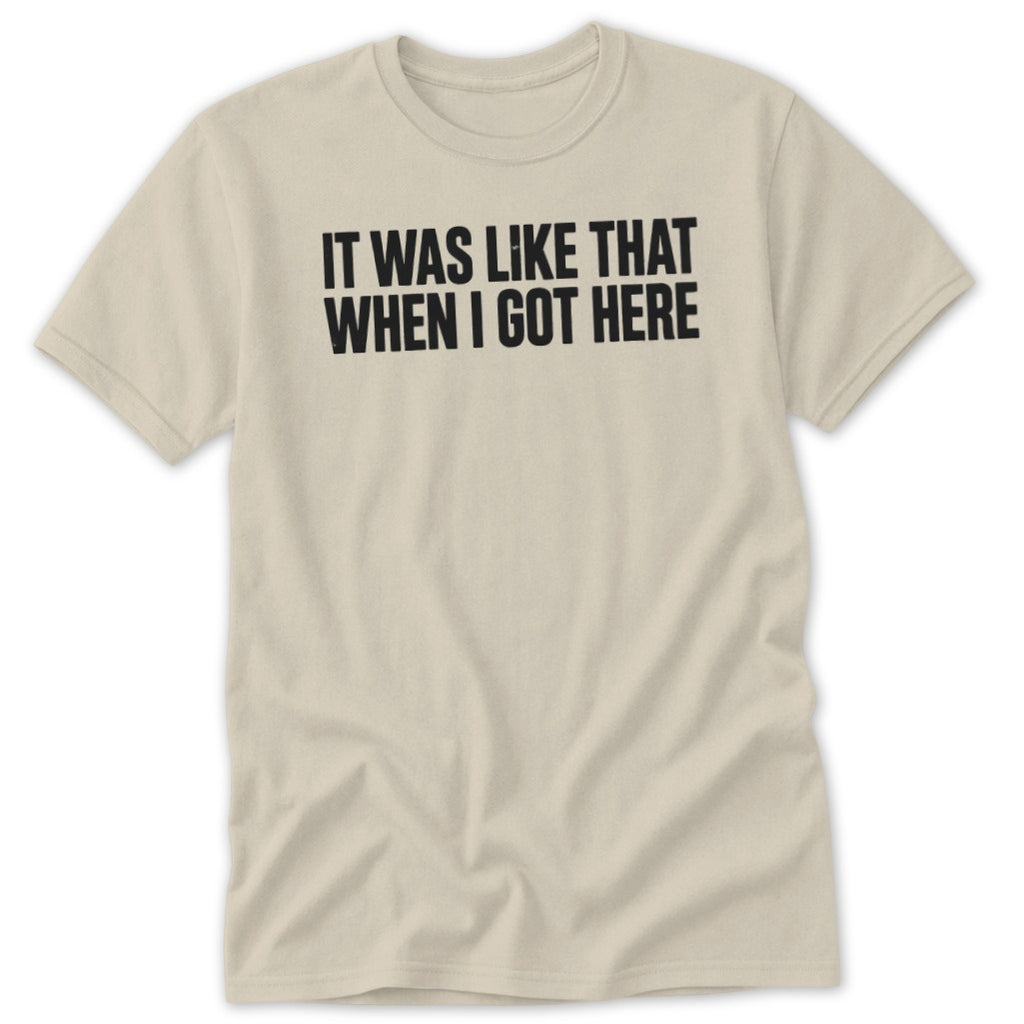 Light tan t-shirt with black text "IT WAS LIKE THAT WHEN I GOT HERE".