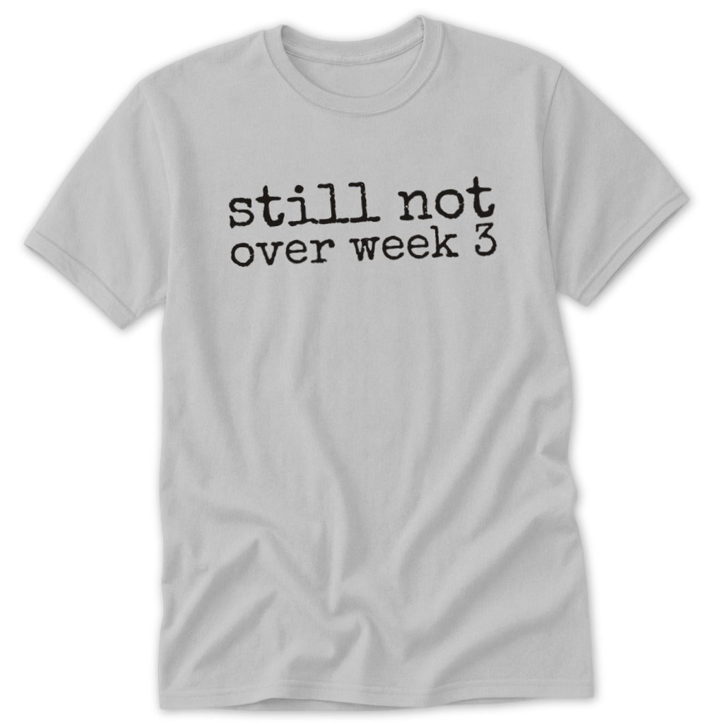 A light grey t-shirt featuring the black text "still not over week 3" printed across the chest.