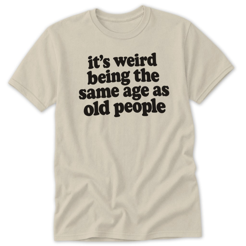 A beige t-shirt printed with the black text "it's weird being the same age as old people".