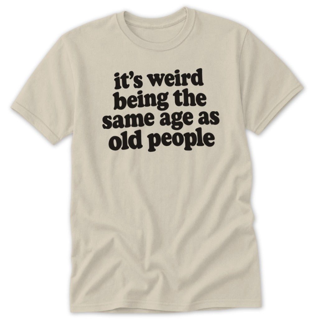 A beige t-shirt printed with the black text "it's weird being the same age as old people".