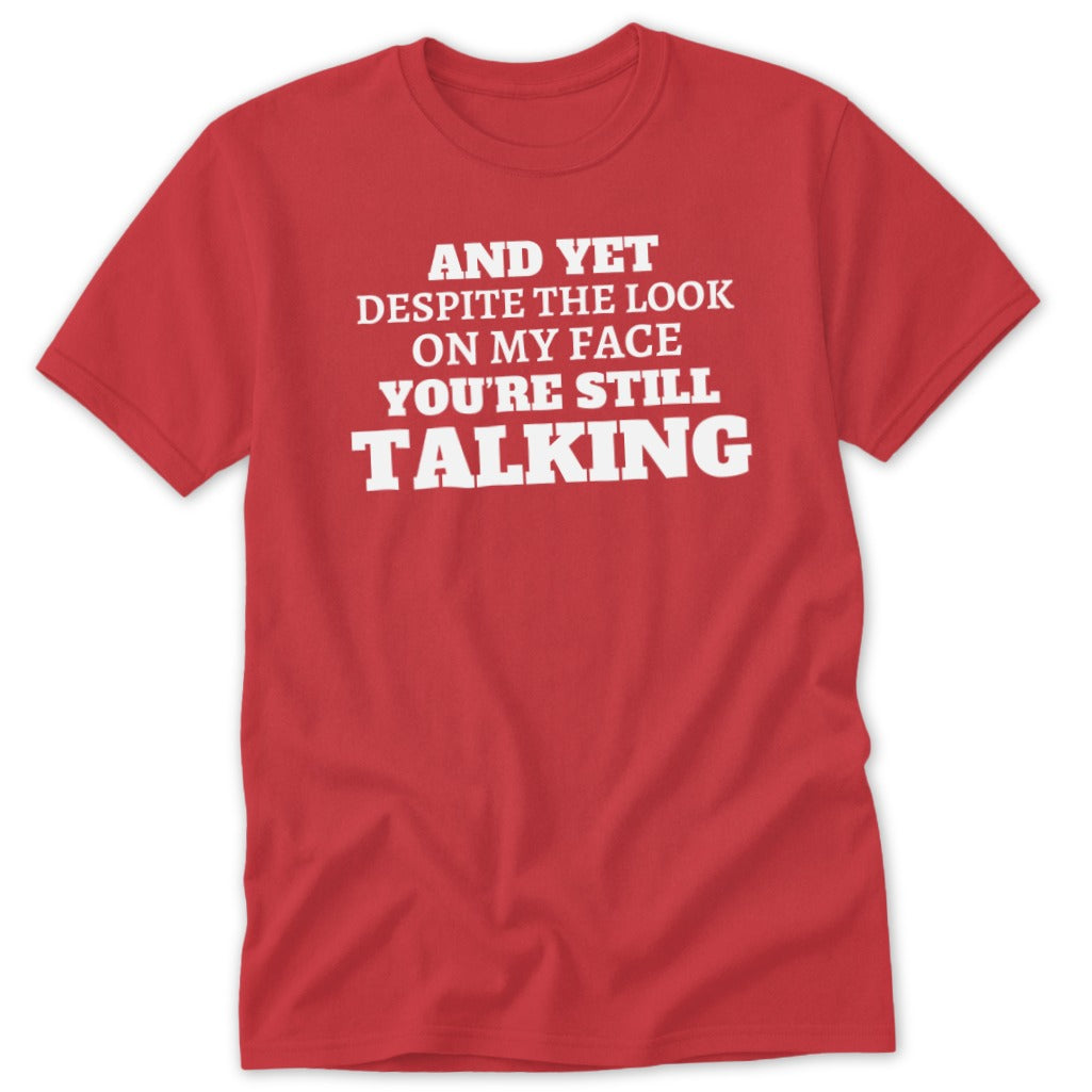Red t-shirt with white text: "AND YET DESPITE THE LOOK ON MY FACE YOU'RE STILL TALKING"