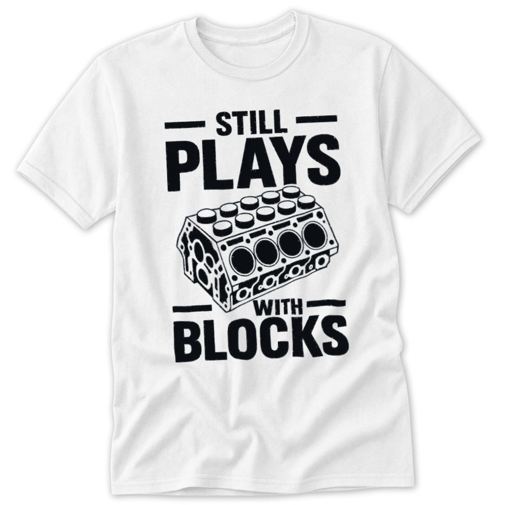 White t-shirt with black text "STILL PLAYS WITH BLOCKS" and engine block graphic.