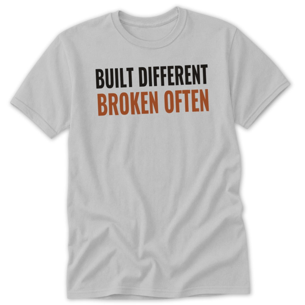 Light gray t-shirt with black text "BUILT DIFFERENT" and orange text "BROKEN OFTEN".