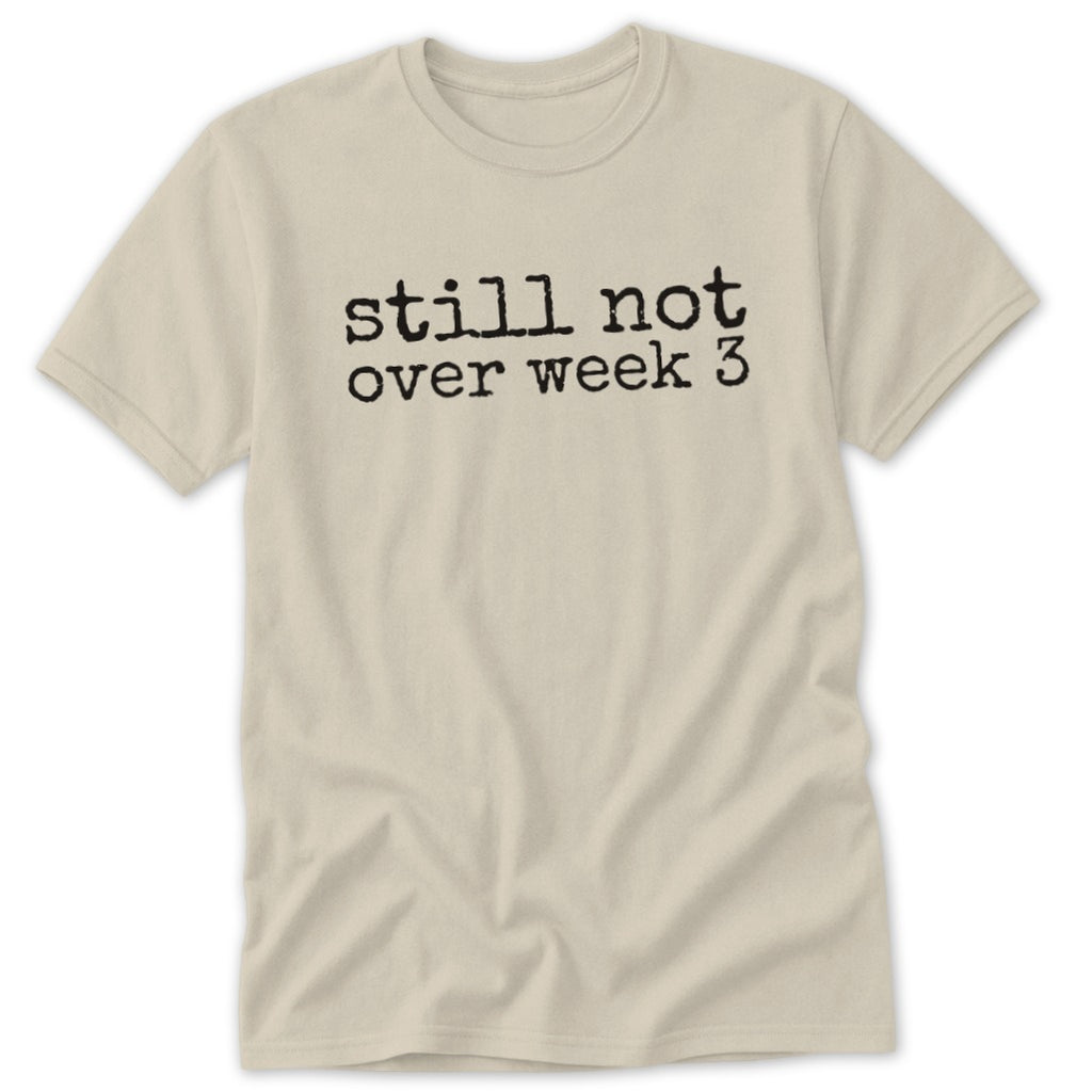 A light beige short-sleeve crewneck t-shirt with the black typewriter text still not over week 3 centered on the chest.