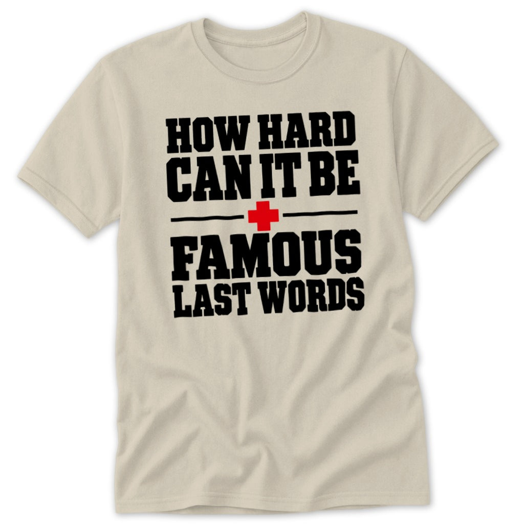 A cream-colored short-sleeved t-shirt featuring black block lettering that reads HOW HARD CAN IT BE FAMOUS LAST WORDS with a red cross icon in the center.