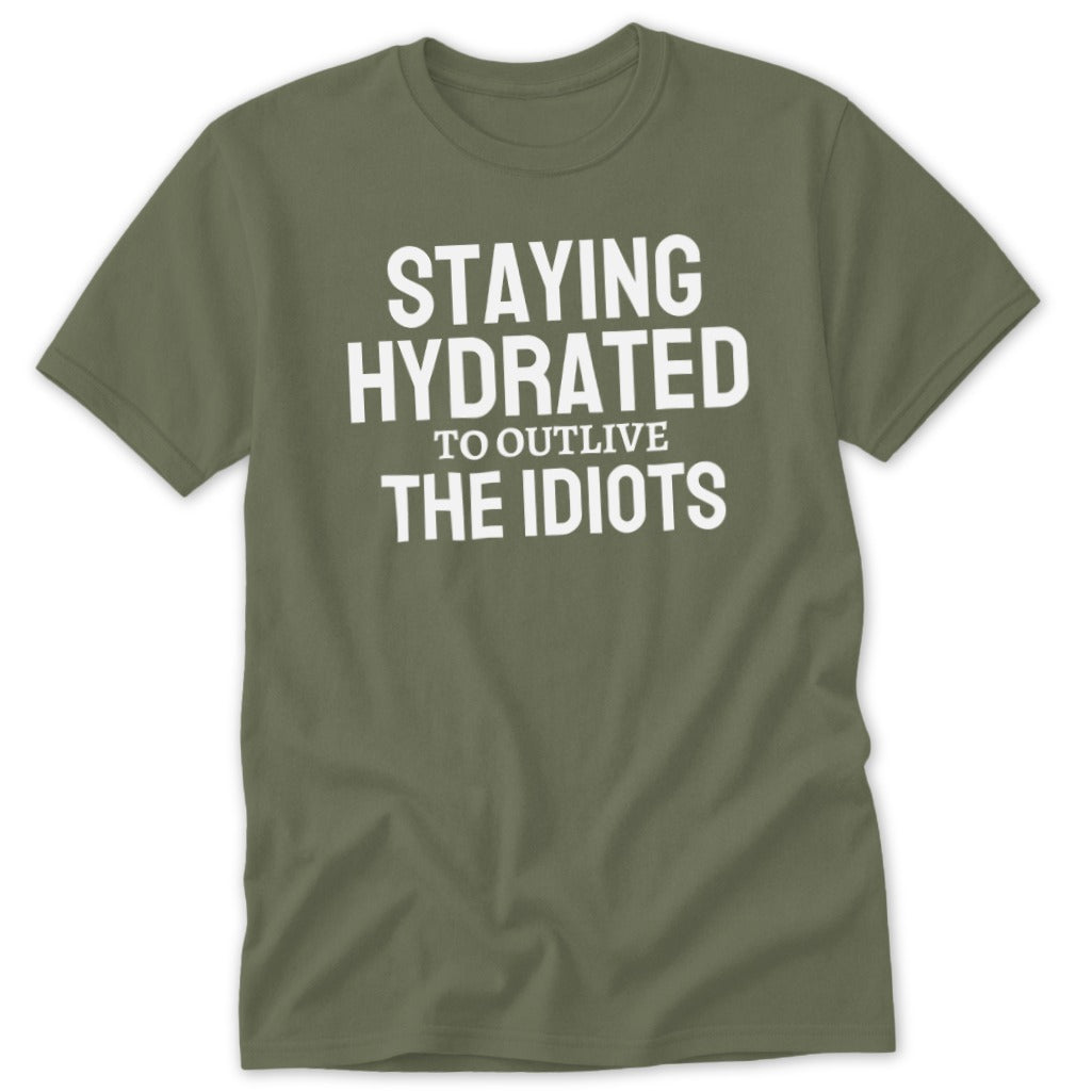 Olive green t-shirt with white text reading "STAYING HYDRATED TO OUTLIVE THE IDIOTS."