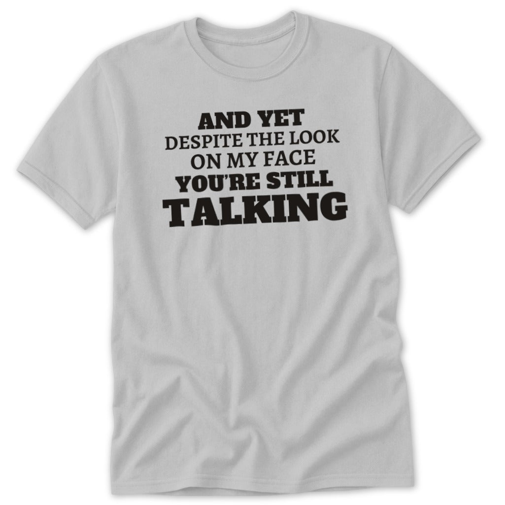Grey t-shirt with black text: "AND YET DESPITE THE LOOK ON MY FACE YOU'RE STILL TALKING".