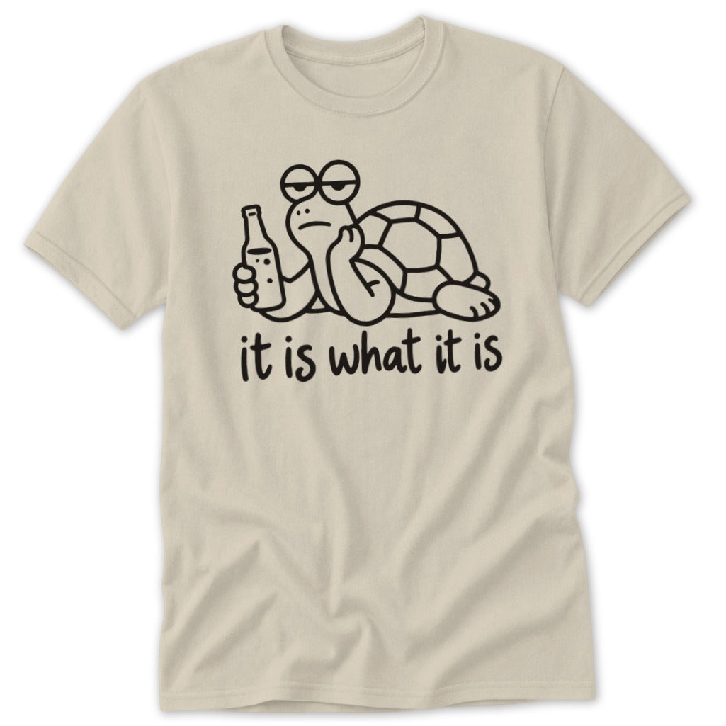 A cream-colored t-shirt with a black line art graphic of a bored turtle holding a bottle, accompanied by the text it is what it is.