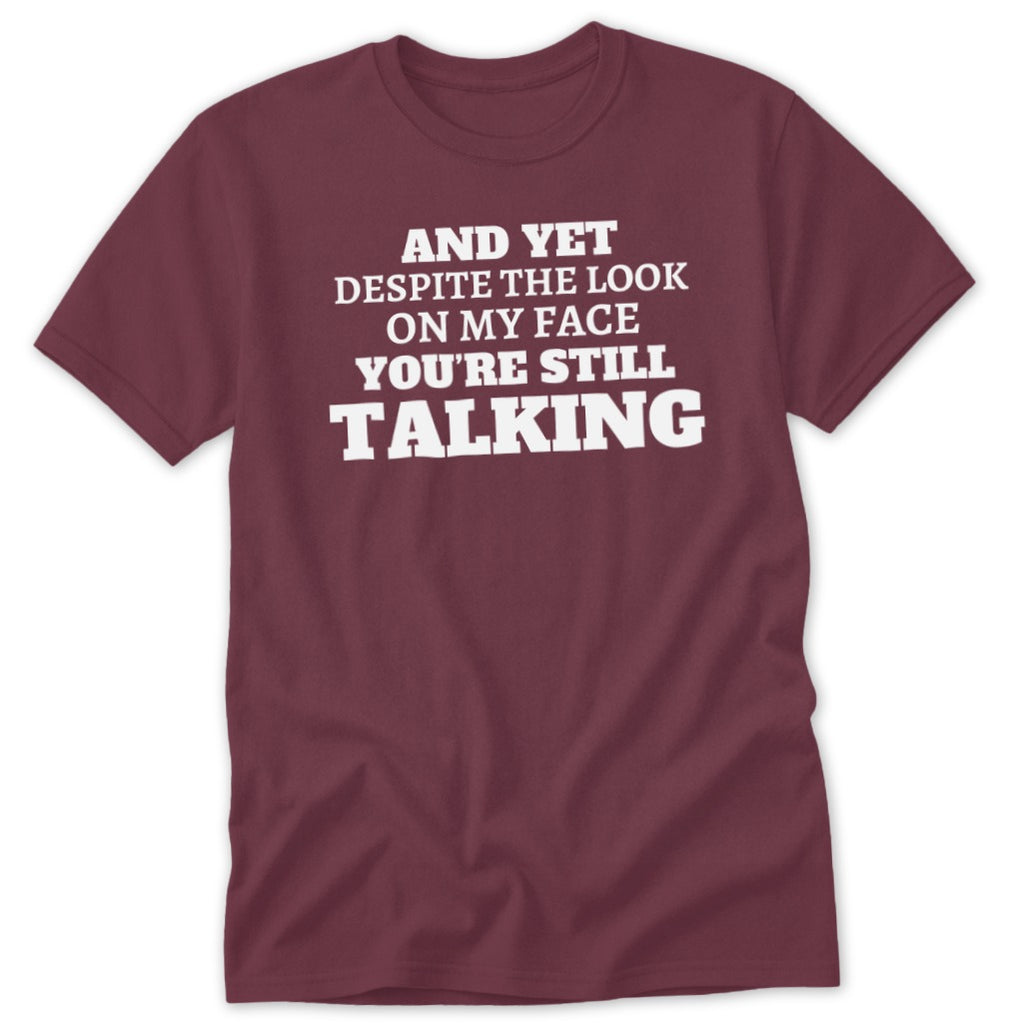 Maroon t-shirt with white text: "AND YET DESPITE THE LOOK ON MY FACE YOU'RE STILL TALKING".