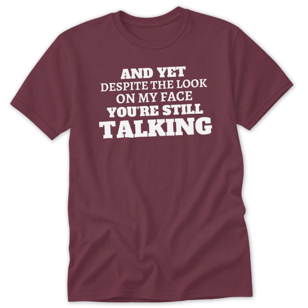 Maroon t-shirt with white text: "AND YET DESPITE THE LOOK ON MY FACE YOU'RE STILL TALKING".