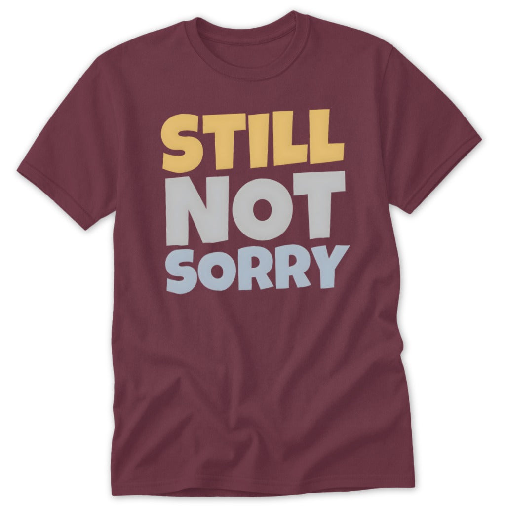 Maroon short-sleeved t-shirt with the text "STILL NOT SORRY" printed in stacked yellow, grey, and light blue letters.