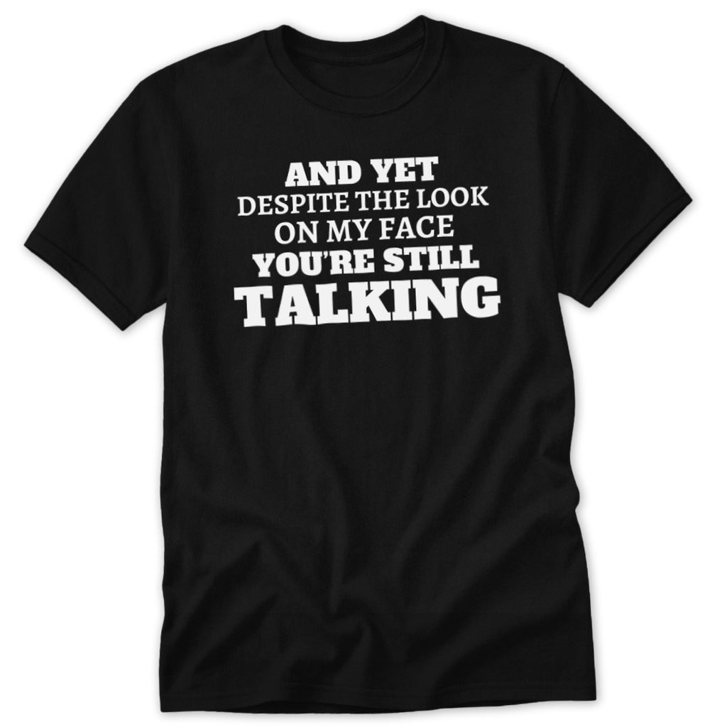Black t-shirt with white text: AND YET DESPITE THE LOOK ON MY FACE YOU'RE STILL TALKING.