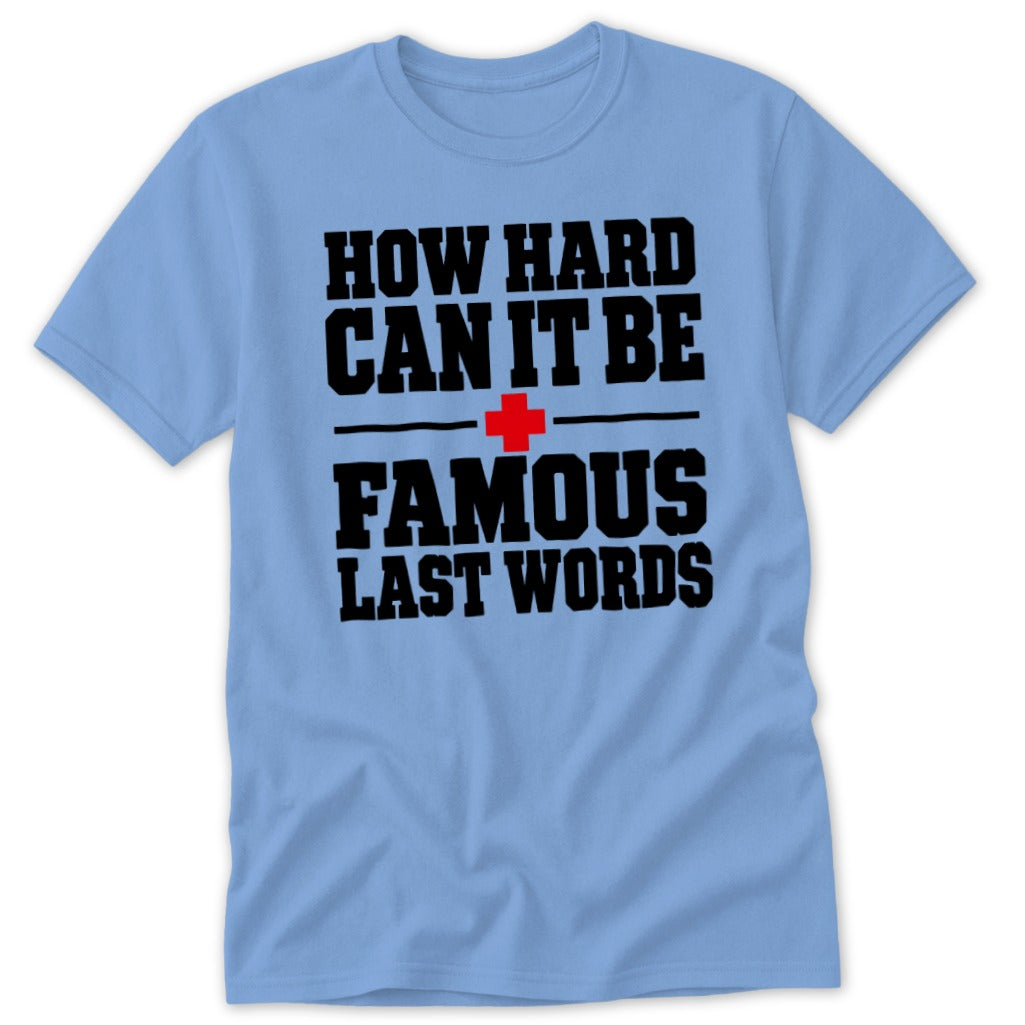 Light blue short-sleeve t-shirt with black text that reads HOW HARD CAN IT BE FAMOUS LAST WORDS and a red cross symbol.