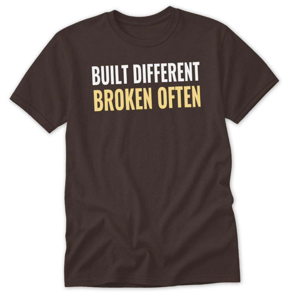 Brown t-shirt with white and yellow text reading "BUILT DIFFERENT BROKEN OFTEN".