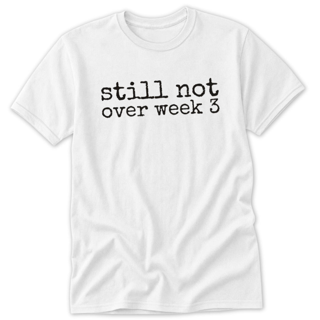 A white t-shirt featuring the black typewriter-style text still not over week 3 centered on the chest.