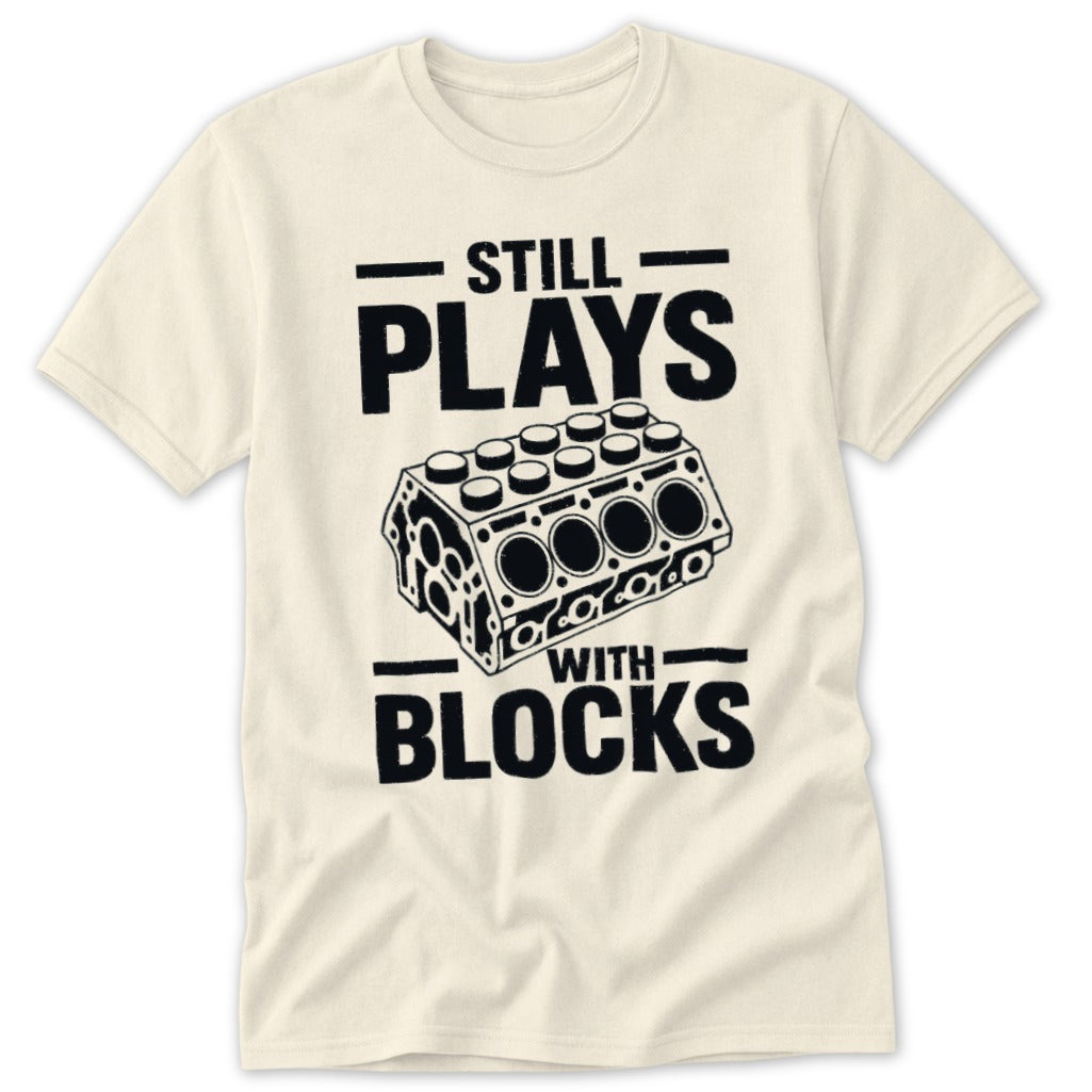 Cream t-shirt with black text and graphics: "STILL PLAYS WITH BLOCKS" and engine block illustration.