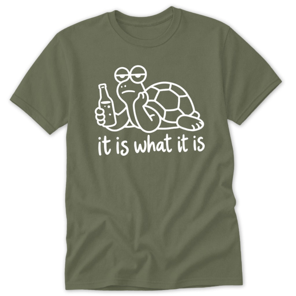 An olive green t-shirt featuring a white line drawing of a lethargic turtle holding a bottle, with the text it is what it is below.