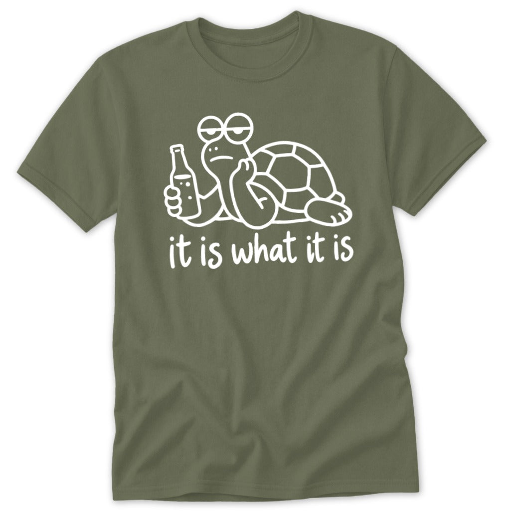 An olive green t-shirt featuring a white line drawing of a lethargic turtle holding a bottle, with the text it is what it is below.