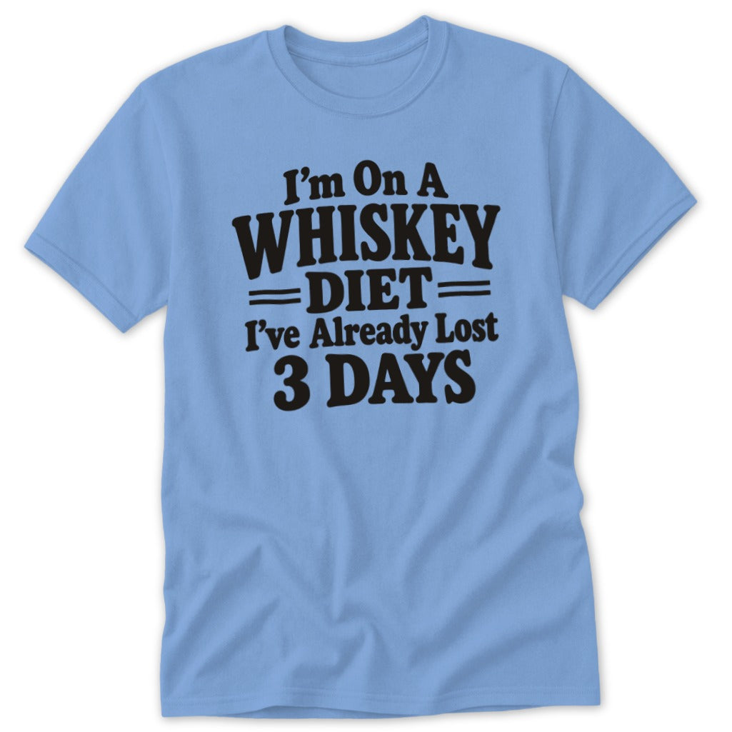 A light blue crewneck t-shirt featuring black text reading "I'm on a whiskey diet I've already lost 3 days."