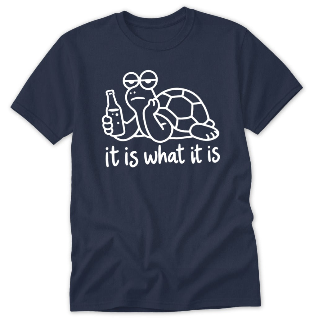 A navy blue t-shirt printed with a white graphic of a turtle holding a bottle, accompanied by the text it is what it is.
